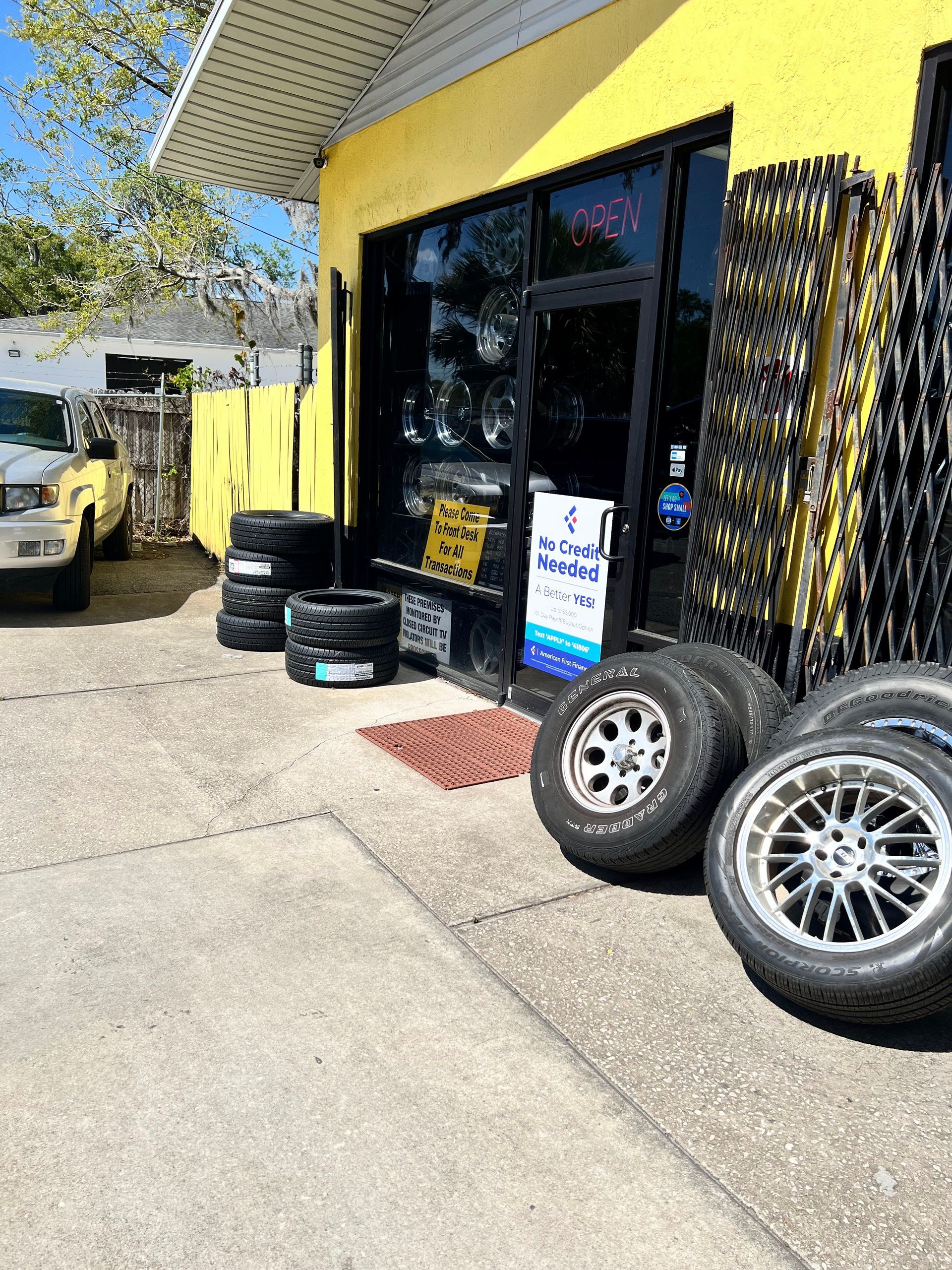 Tire shop with tires displayed outside, yellow building, black door, and a light-colored truck.