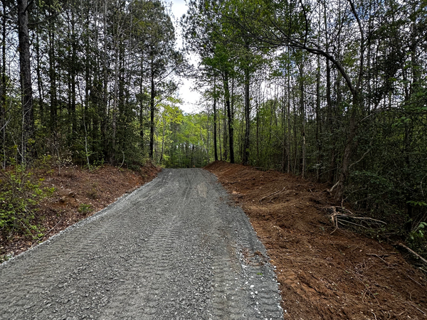 A gravel road going through a forest with trees on both sides.