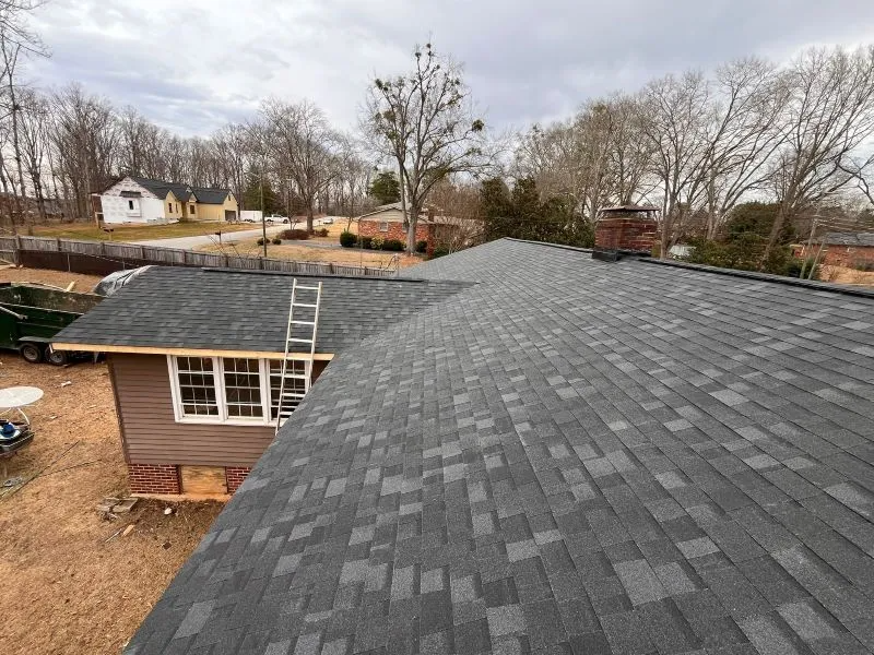 Roof replacement on a house with dark gray shingles and bare trees in the background
