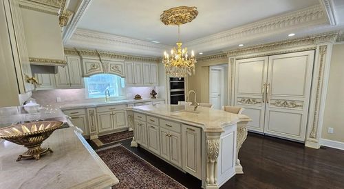 Elegant white kitchen with ornate cabinetry, island, chandelier, and dark hardwood floor