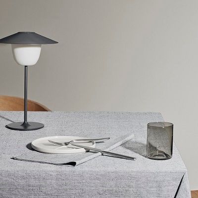 Een tafel met een lamp, borden, bestek en een glas erop.