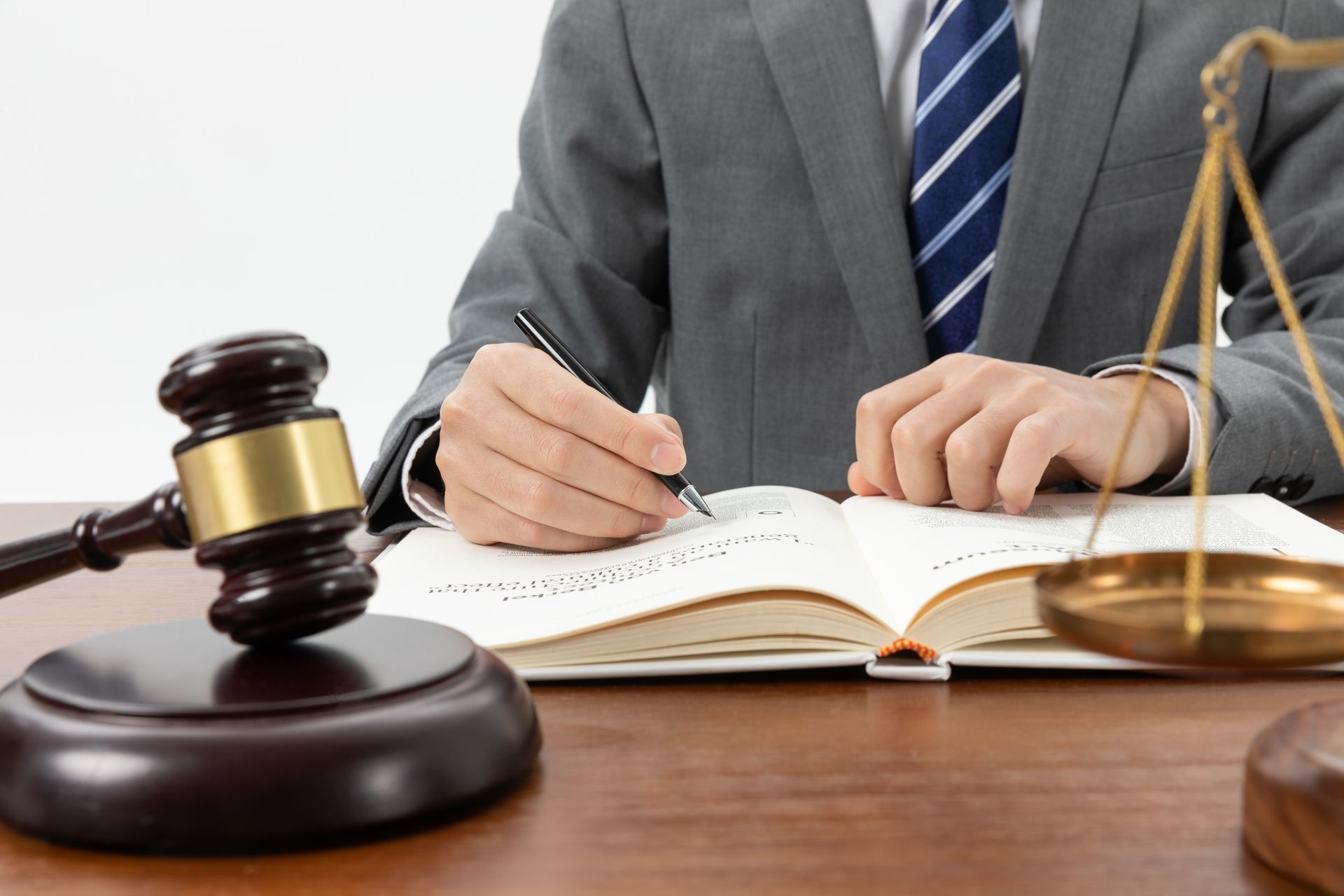 Lawyer in suit writing in a book, gavel, and scales of justice on a wooden desk.