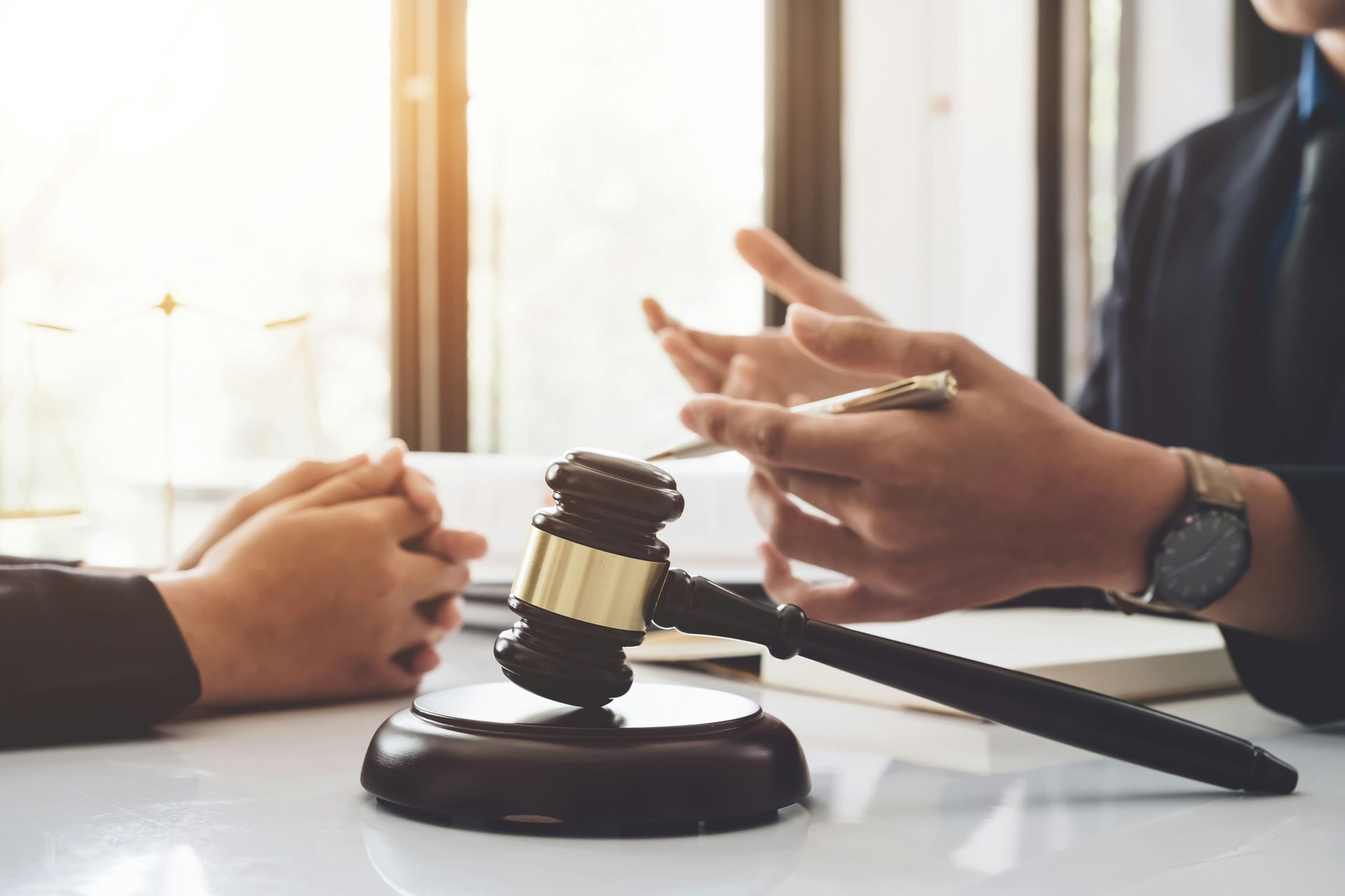 Gavel on desk, two people in suits converse near window.