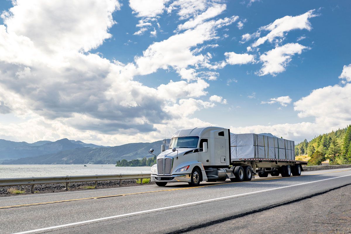 Semi-truck hauling cargo on a highway near a body of water under a cloudy sky.