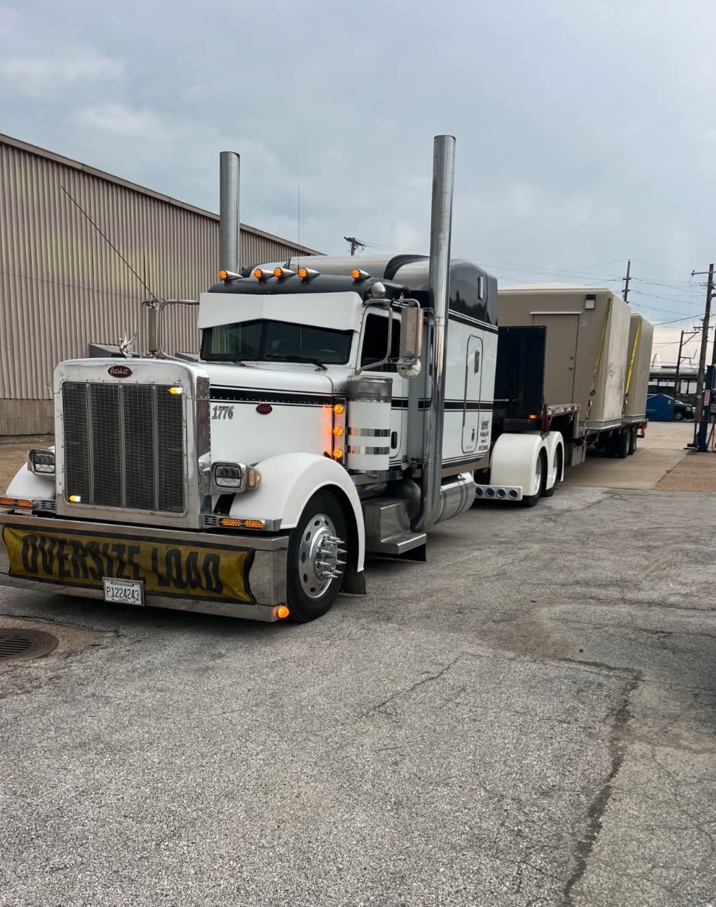 A large silver tanker is transported on a flatbed trailer by a truck on a road under a blue sky.