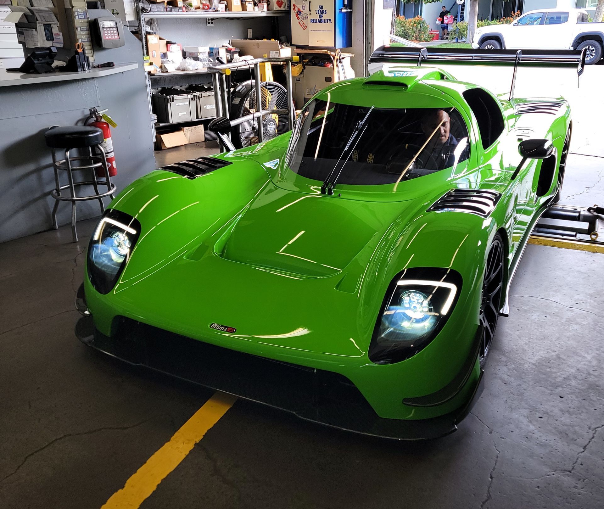Bright green race car in a garage with LED headlights and large rear wing. | Spiteri's Auto Service