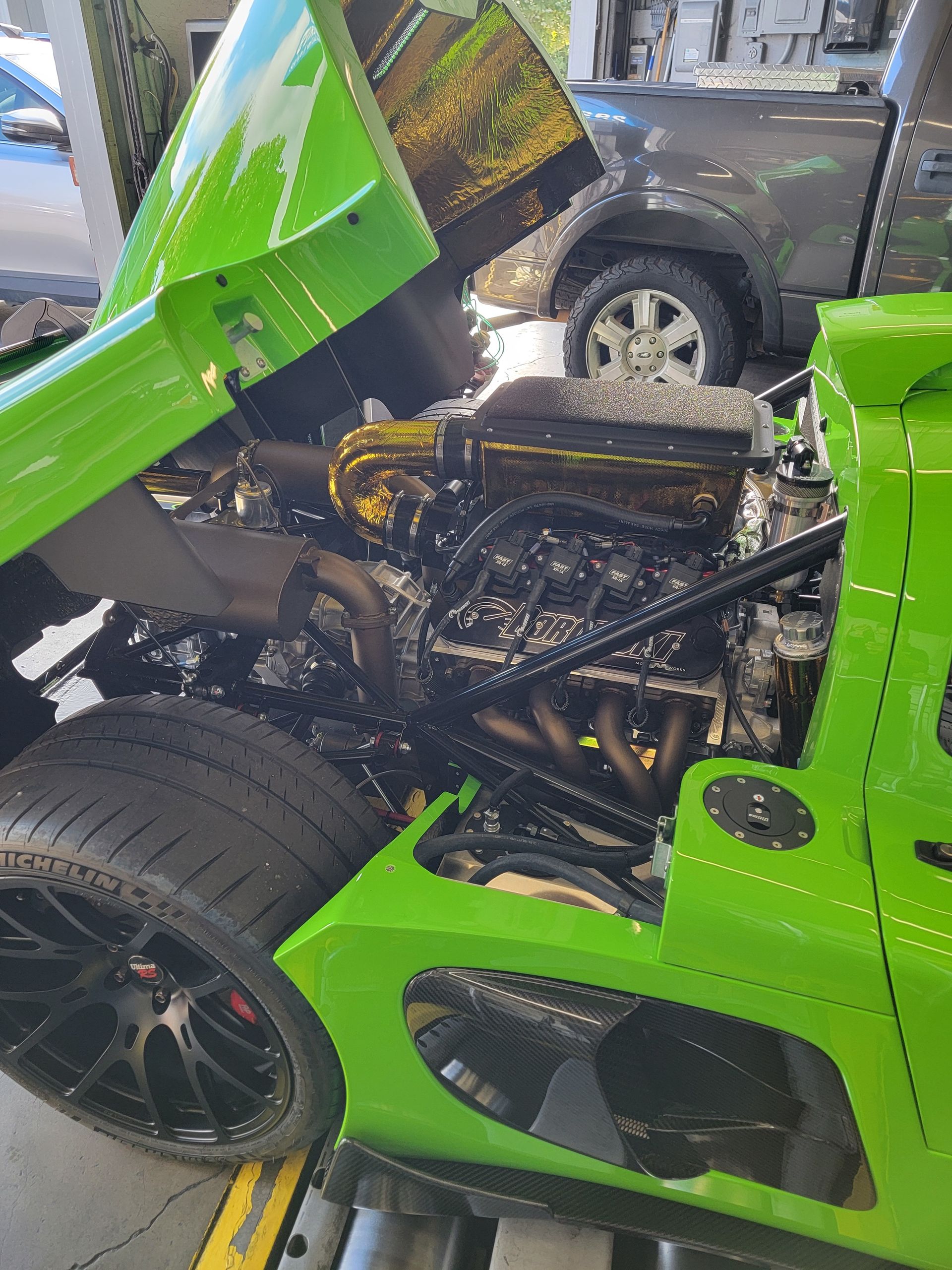 Bright green sports car with engine exposed, likely on a dyno. Black wheels and gold-toned engine components. | Spiteri's Auto Service