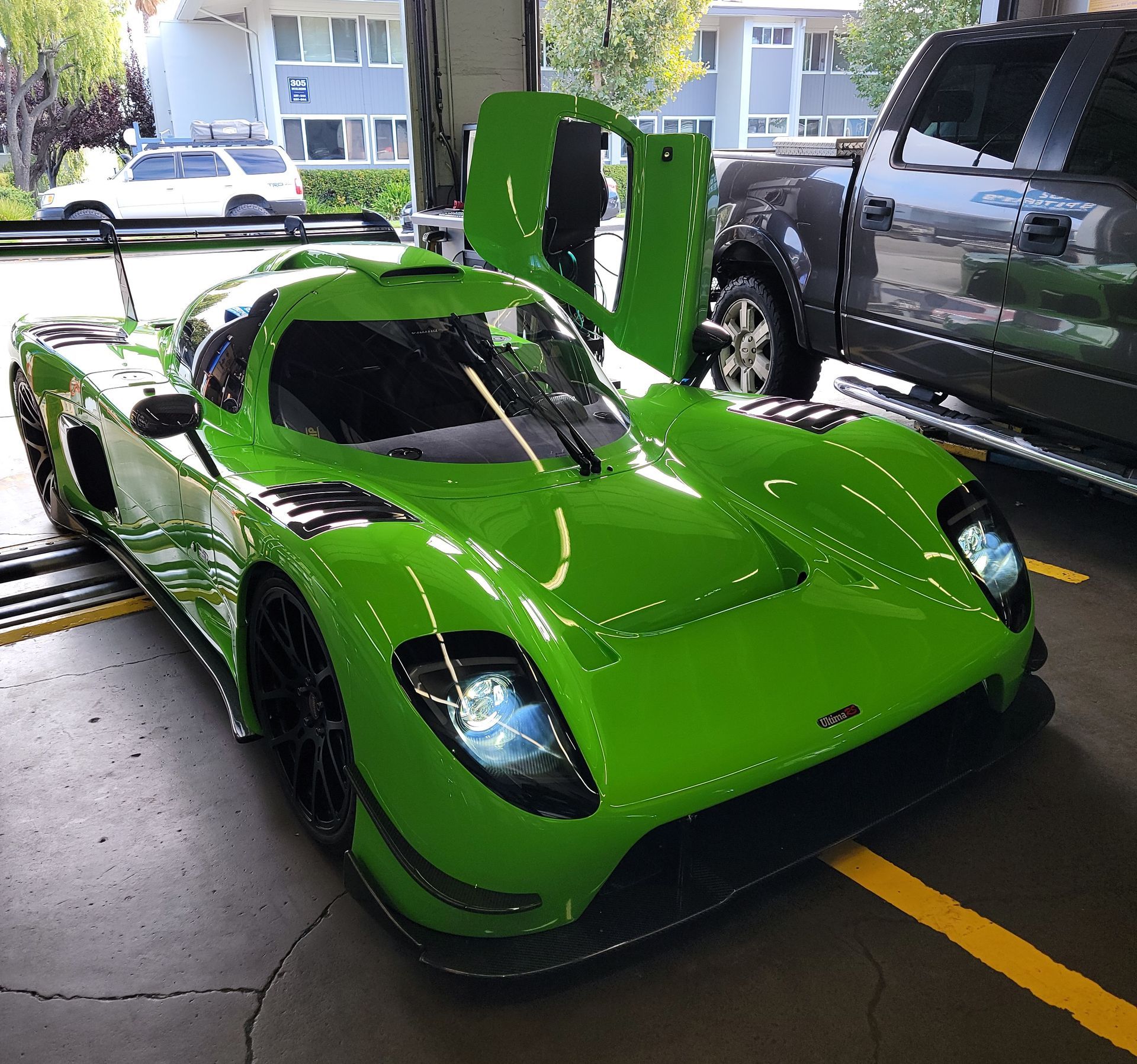 Bright green sports car with door open in a garage, next to a truck. | Spiteri's Auto Service