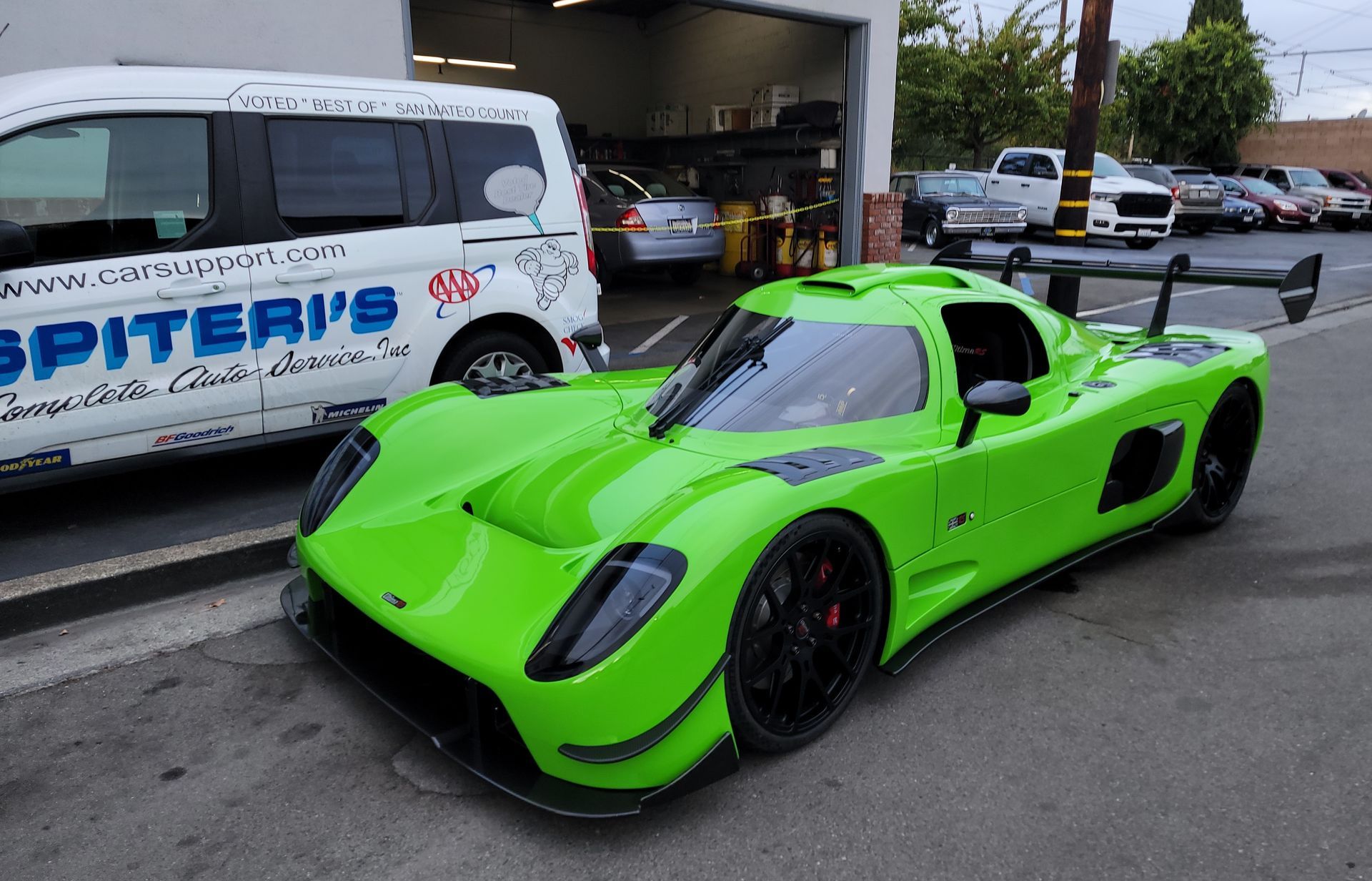 Bright green sports car parked in front of a garage, with a white van to the left. | Spiteri's Auto Service