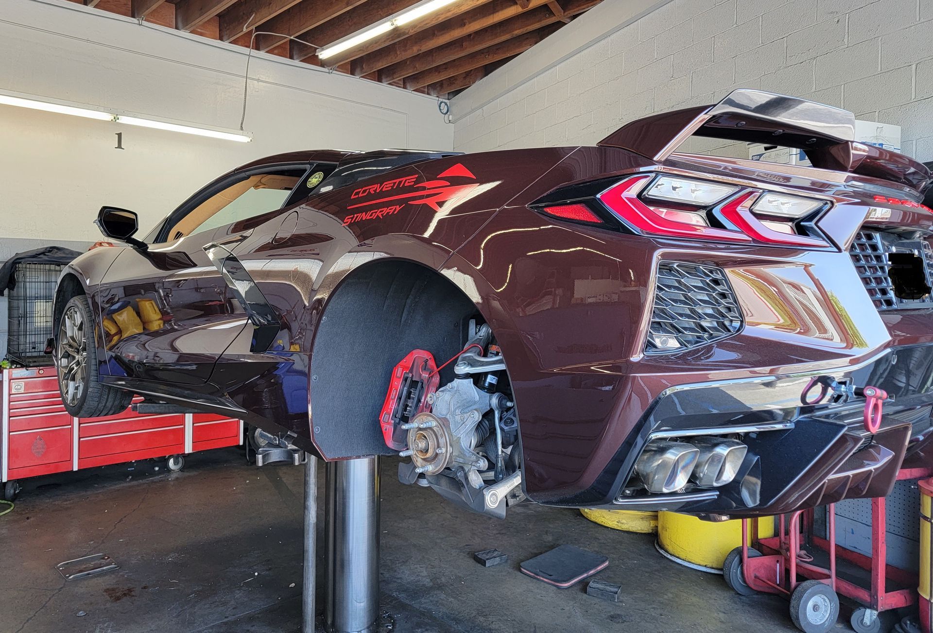 Maroon sports car on a lift in a garage, wheels removed, work in progress. | Spiteri's Auto Service