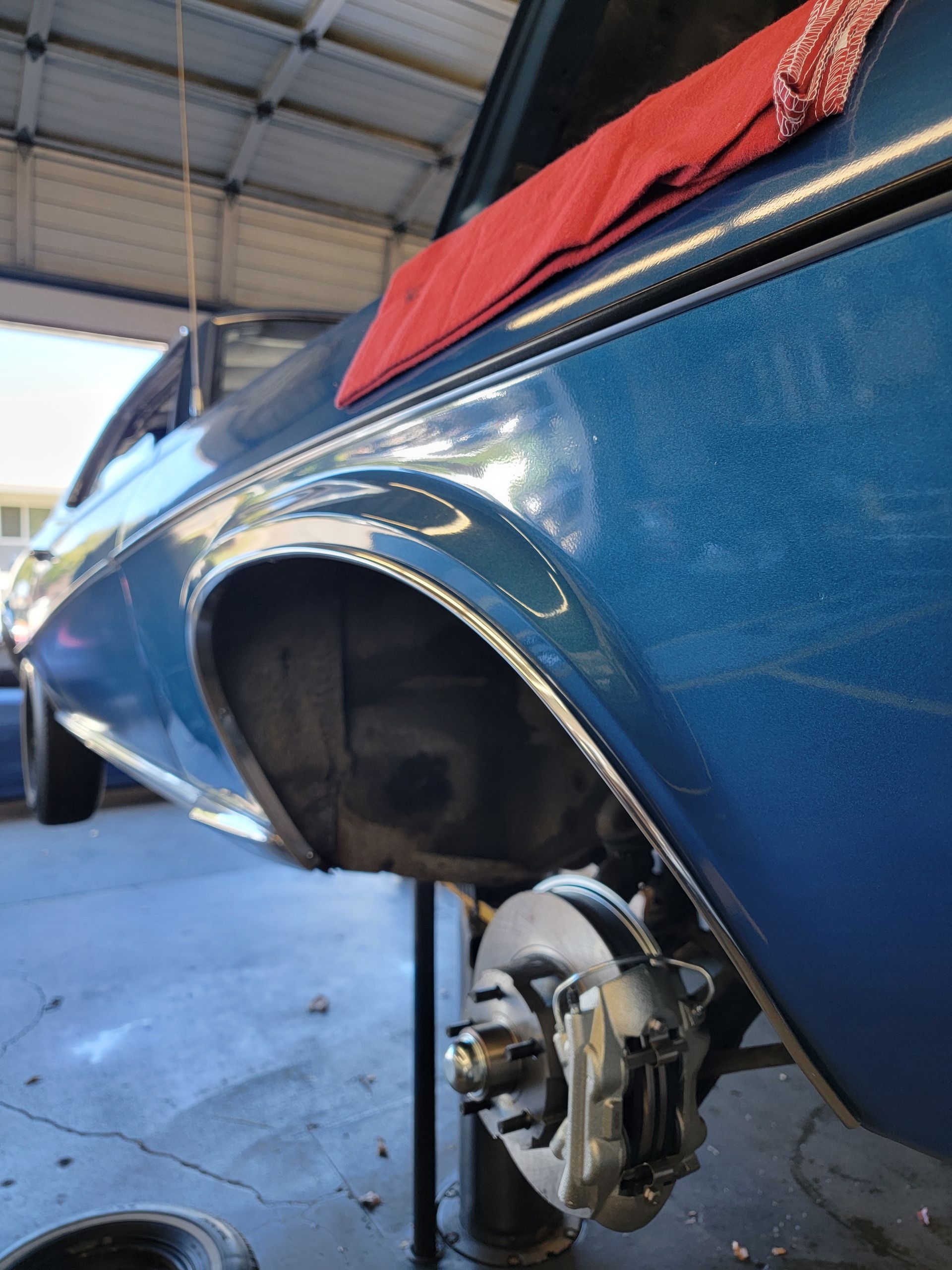 Blue car's rear quarter panel raised on a lift, exposing brake assembly. Red cloth draped across the body. | Spiteri's Auto Service