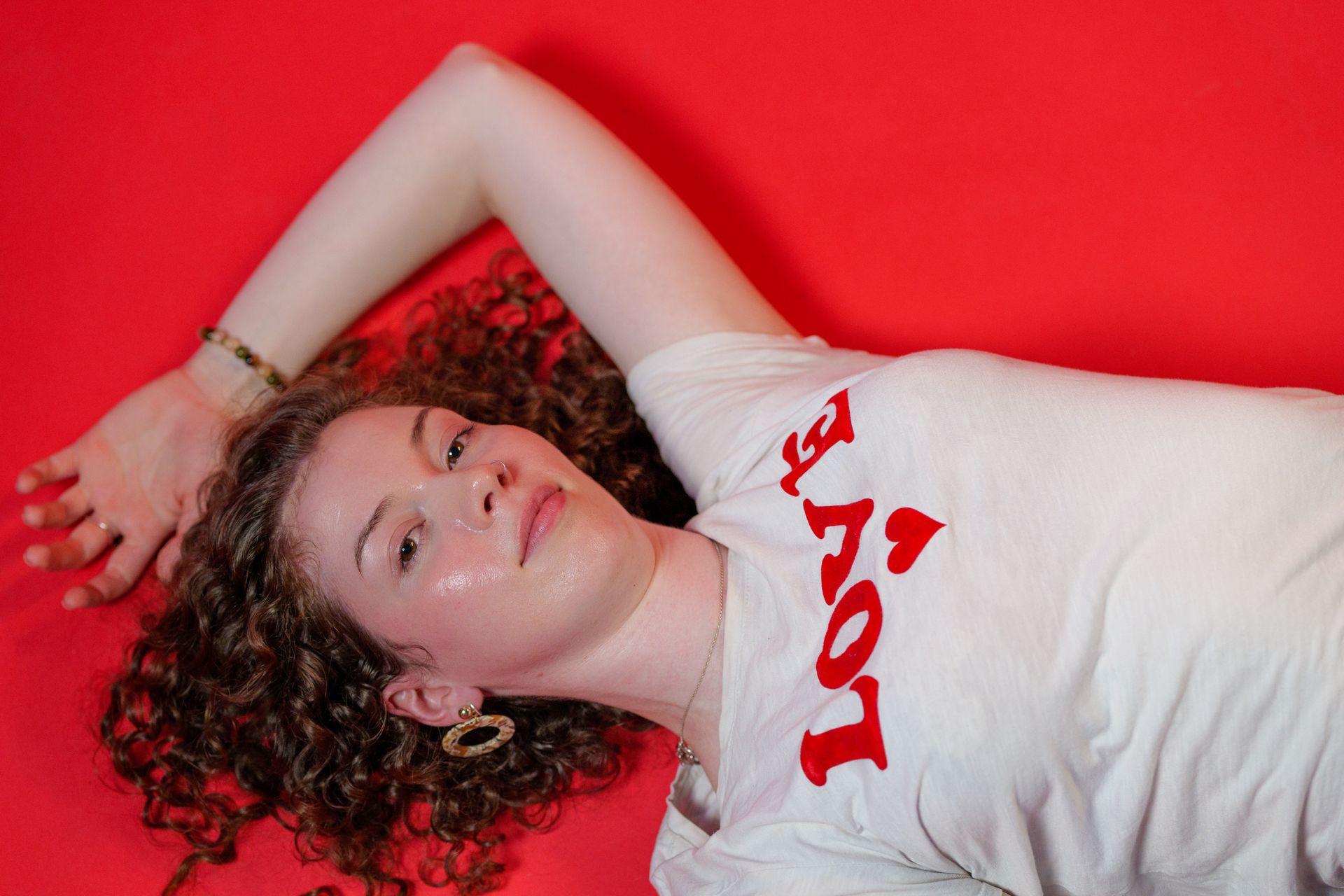 A person with curly hair wearing a white t-shirt with red 