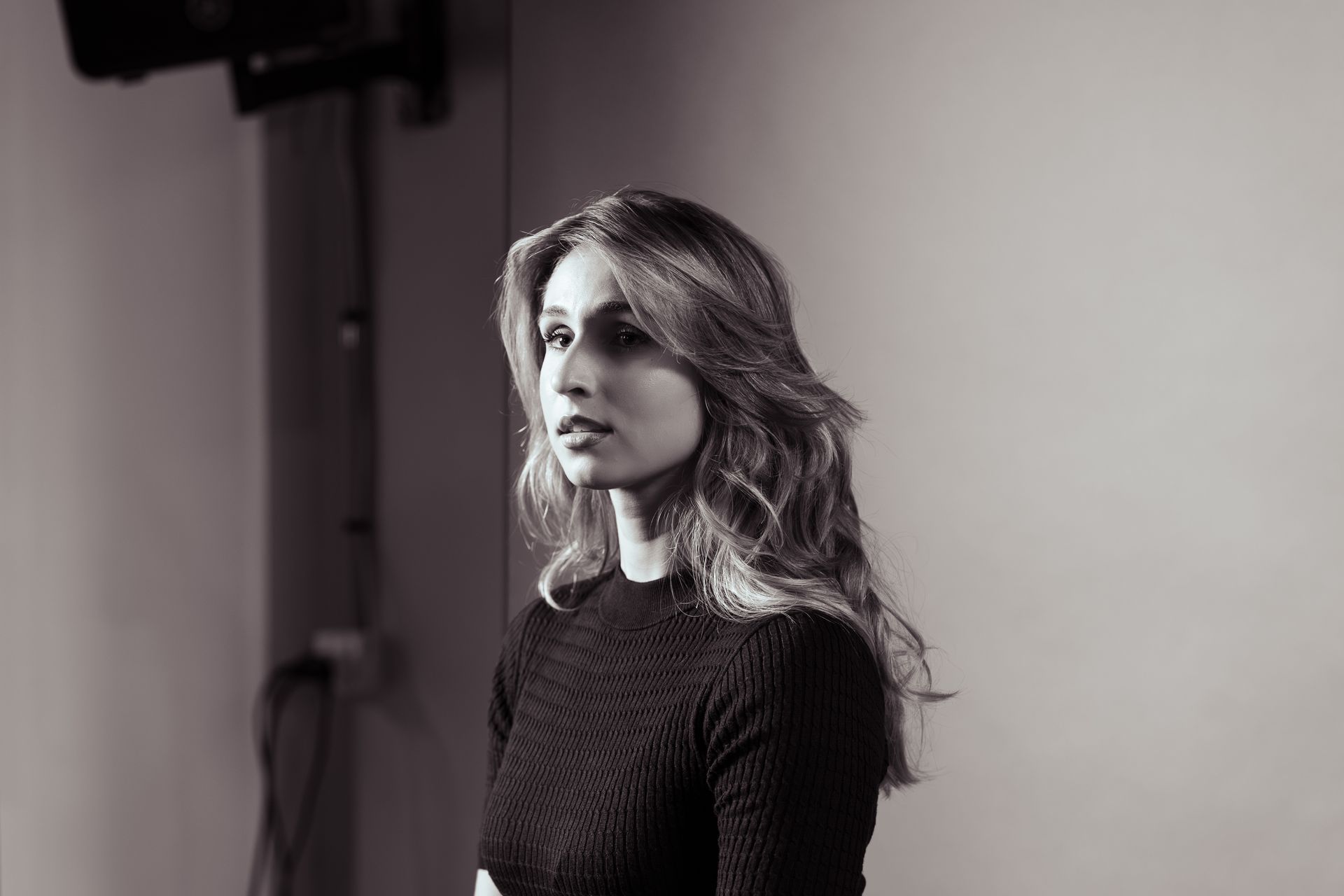 Black and white portrait of a person with long wavy hair, wearing a ribbed top and looking toward the side.