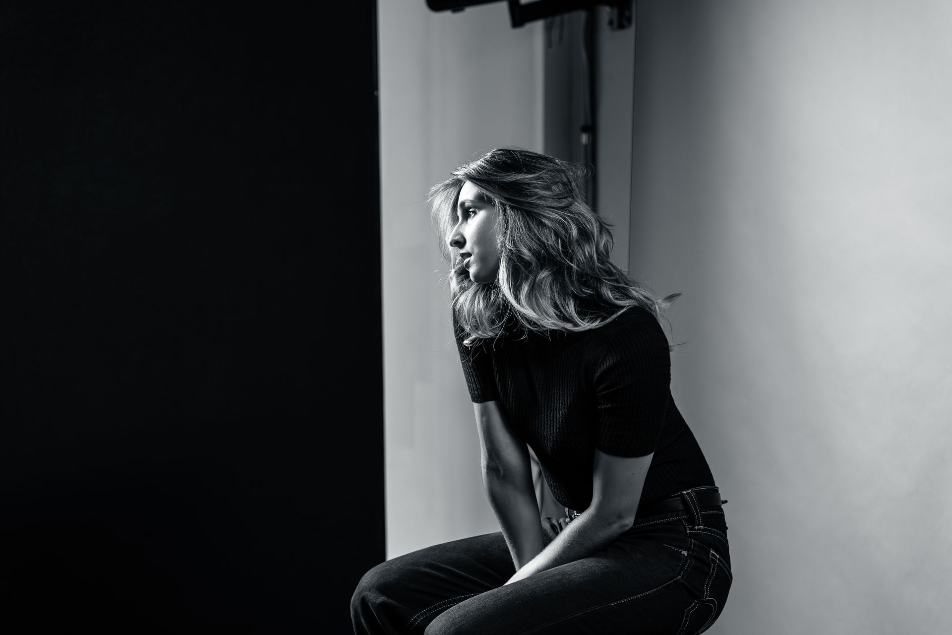 A person with wavy hair sits in profile against a split black and white background, looking thoughtfully to the left.