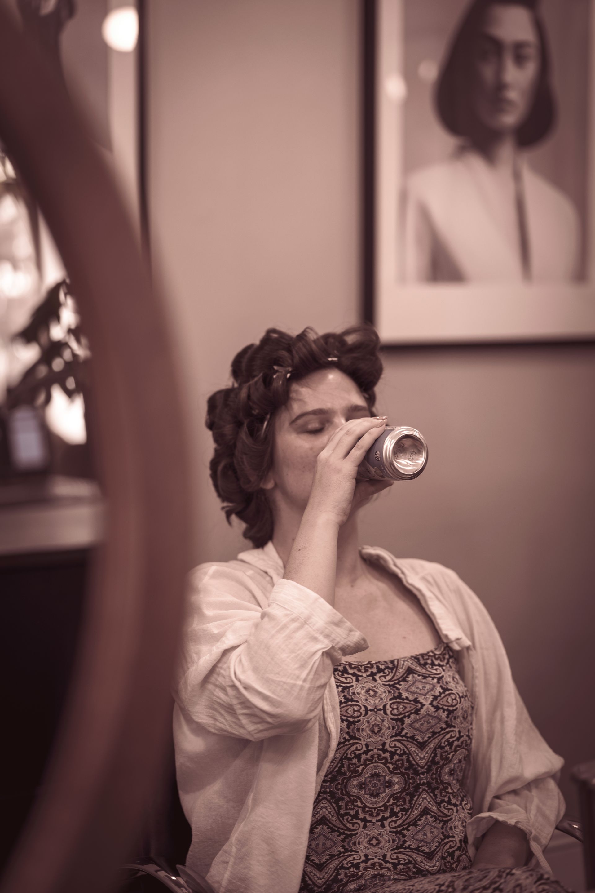A woman is drinking from a can while sitting in a chair.