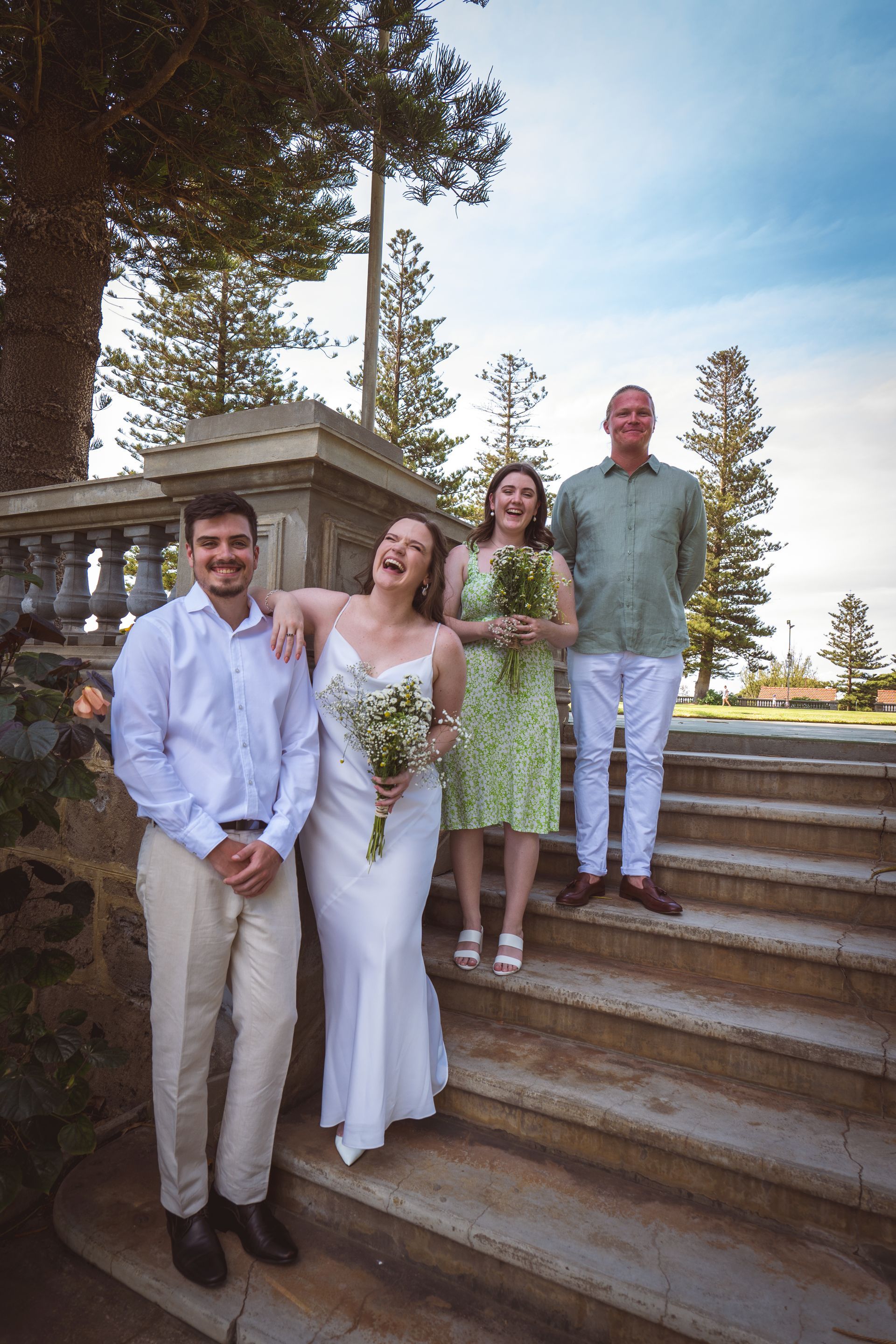 A bride and groom are posing for a picture with their friends on a set of stairs.