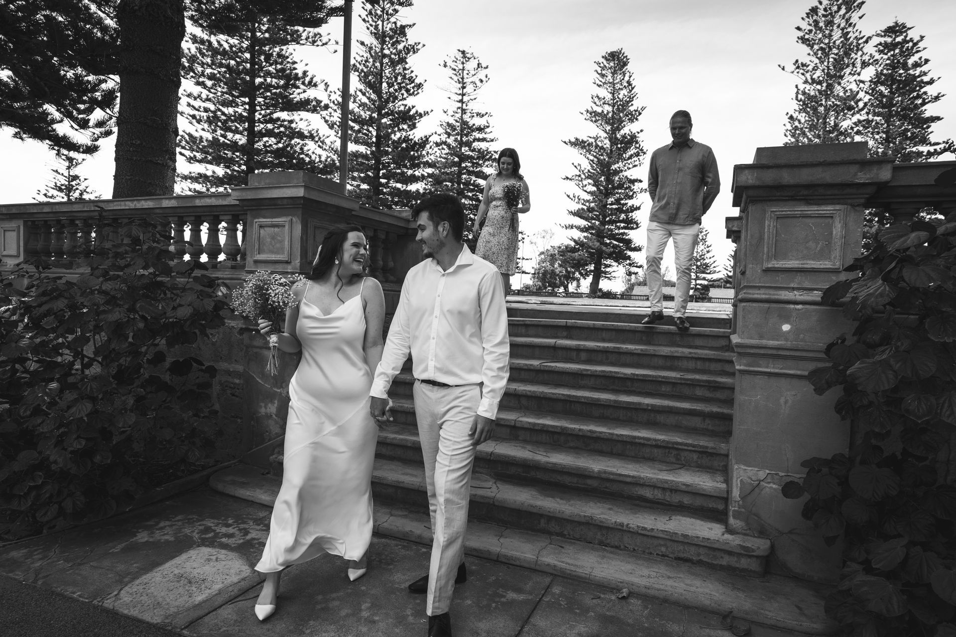 A black and white photo of a bride and groom walking down stairs.
