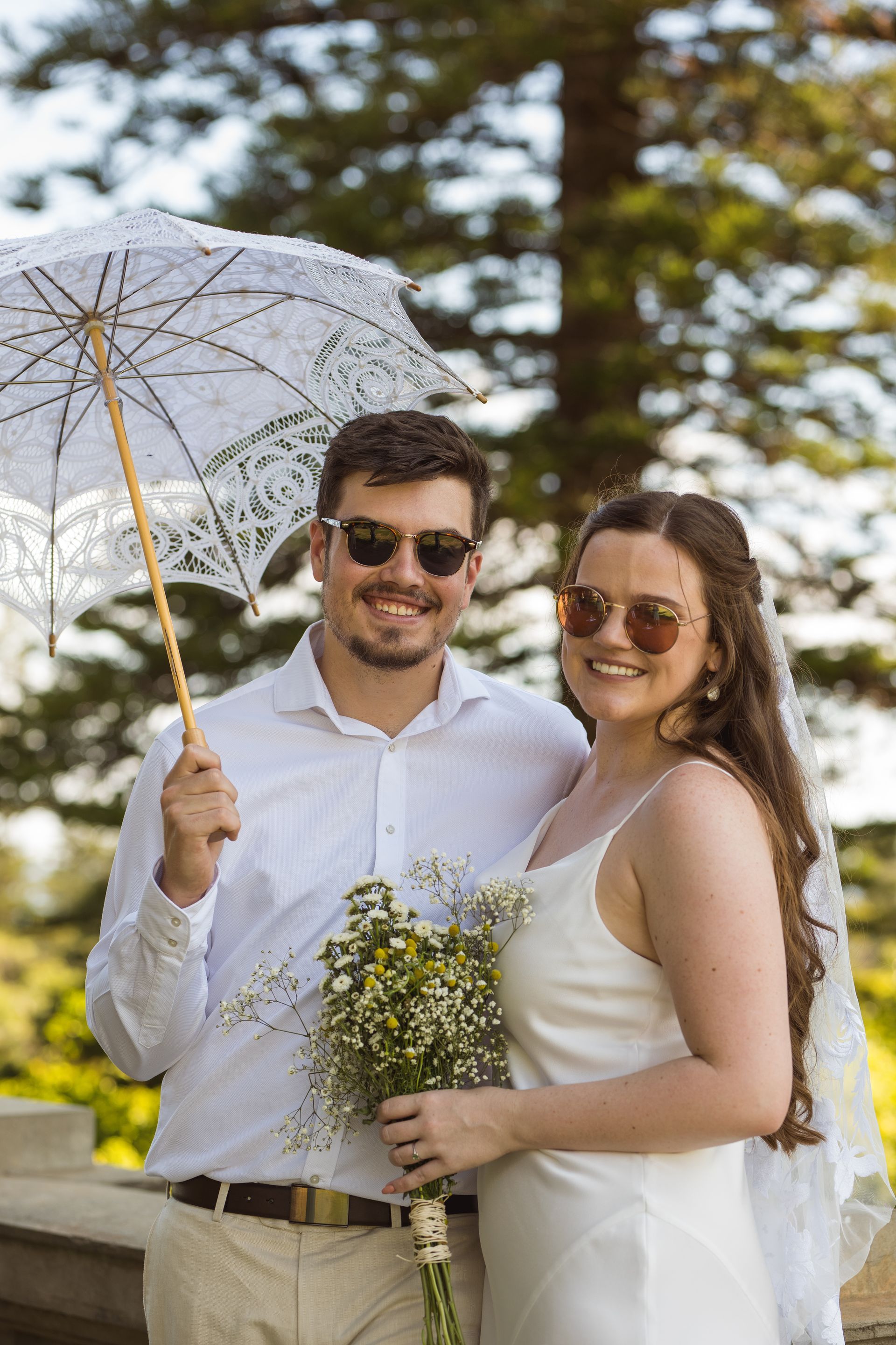 A bride and groom are posing for a picture while holding a parasol.