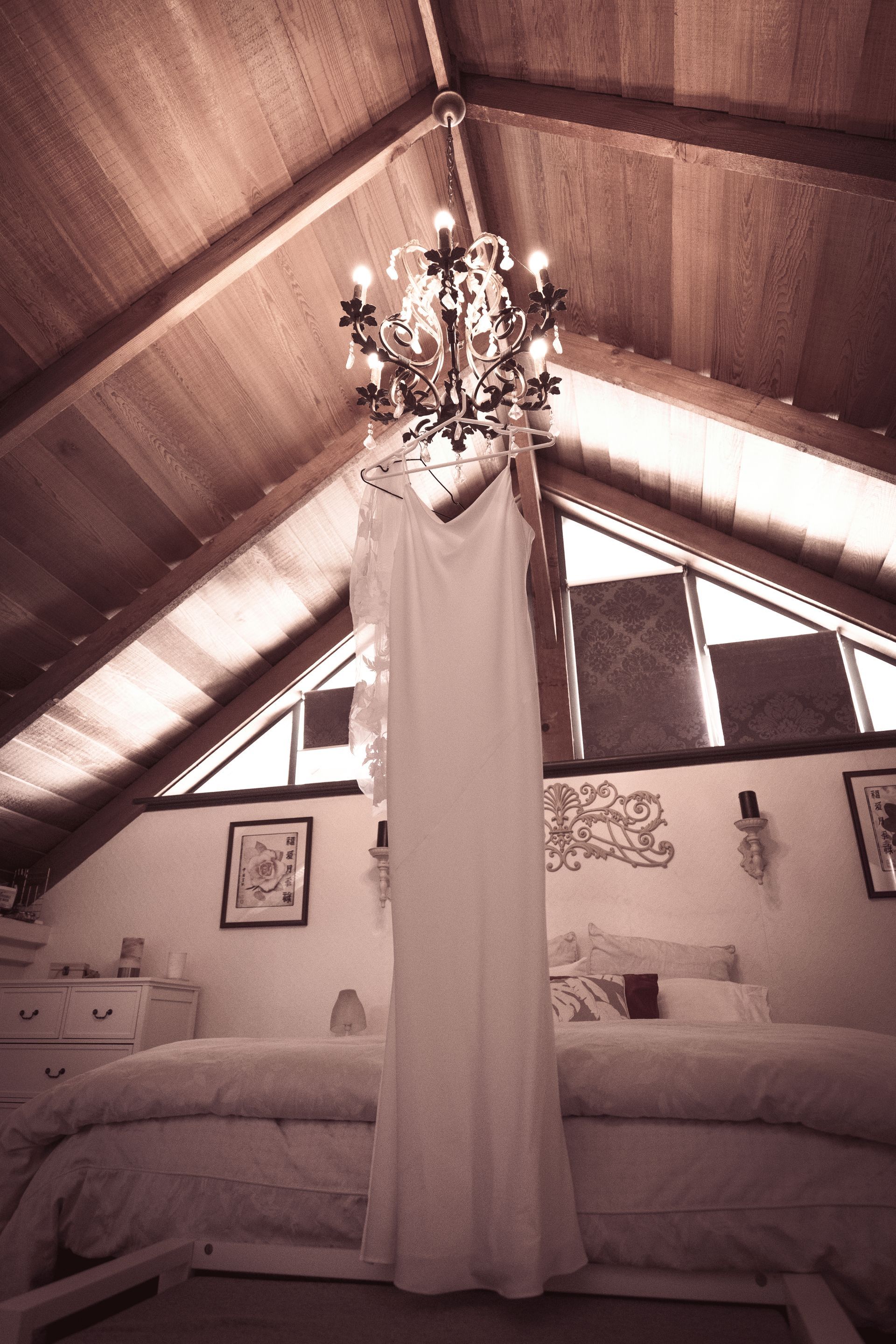 A wedding dress is hanging from a chandelier in a bedroom