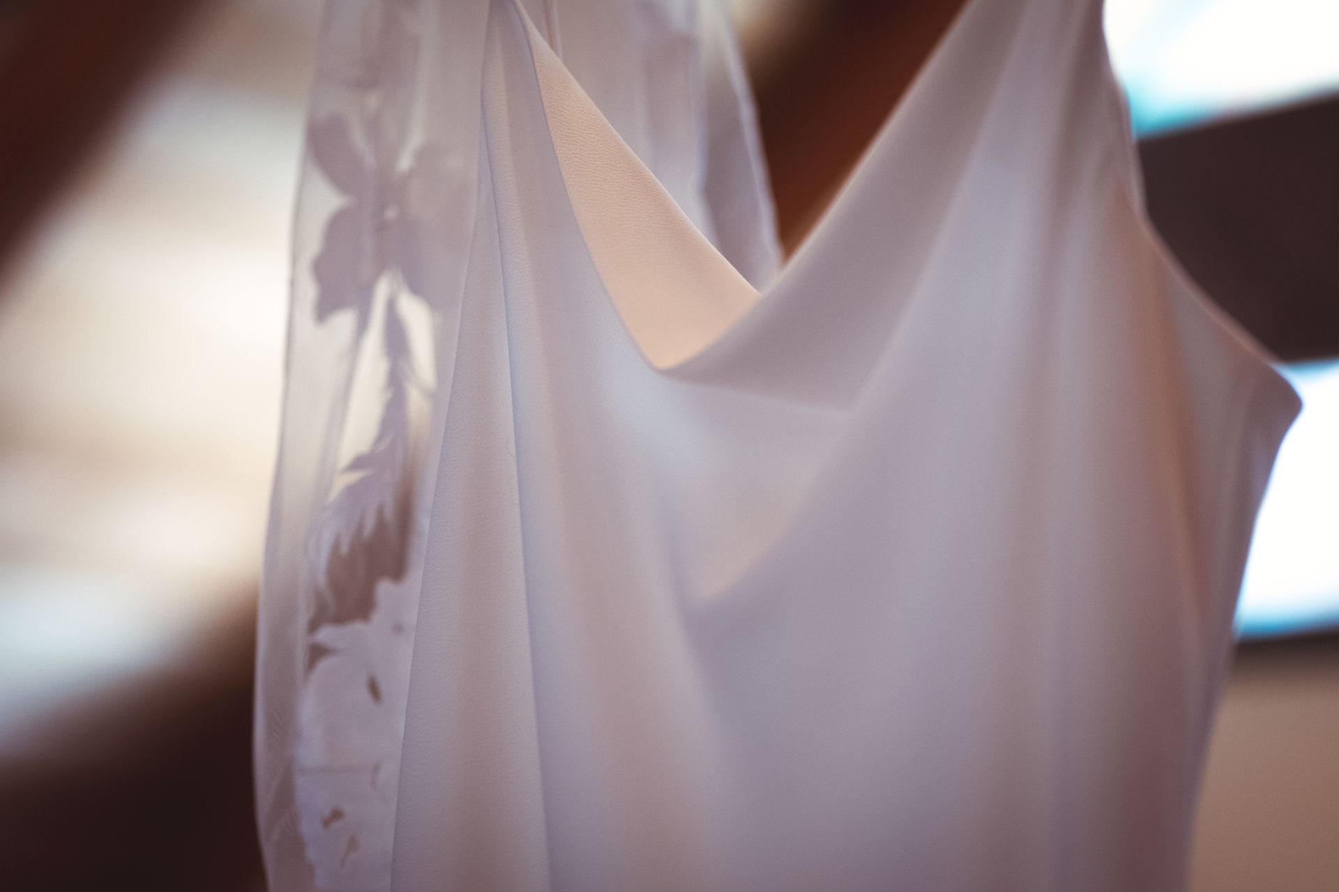 A close up of a white wedding dress hanging on a woman 's shoulder.