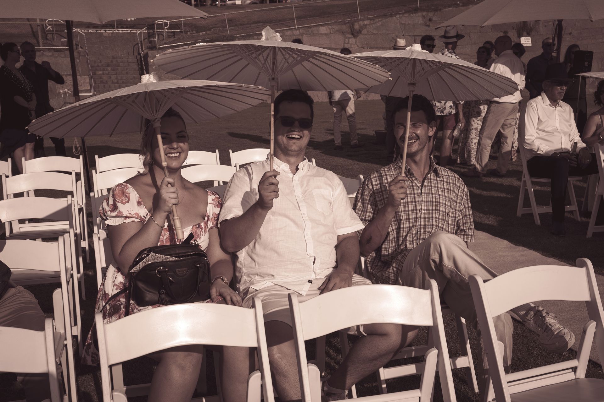 A group of people are sitting under umbrellas in white chairs