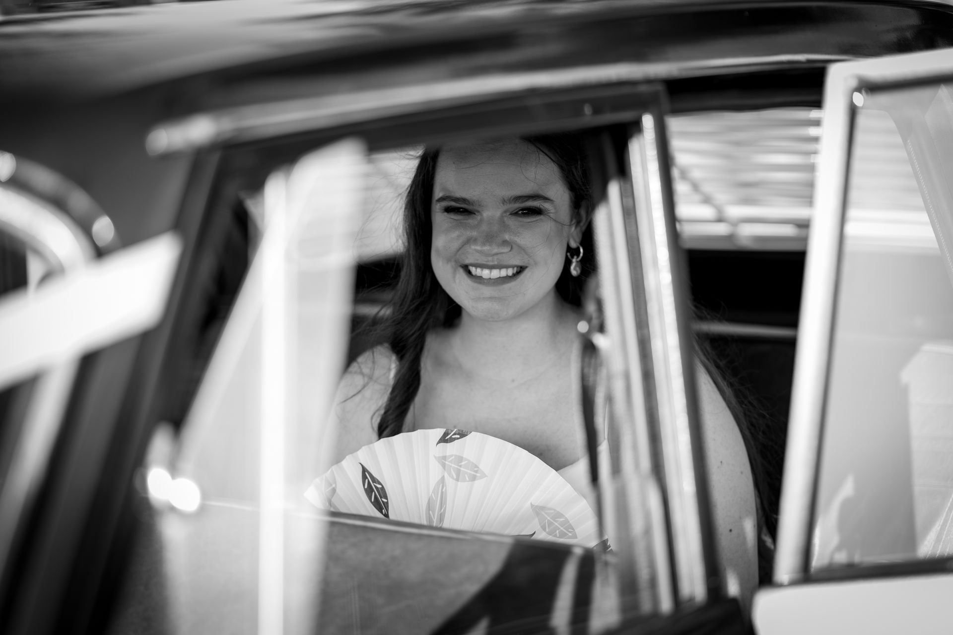 A bride is smiling while sitting in the back seat of a car.