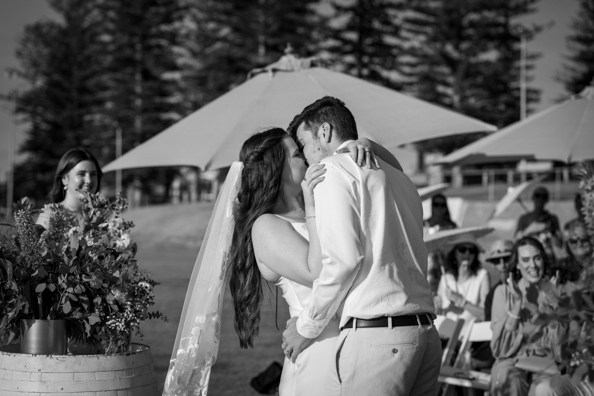 A black and white photo of a bride and groom kissing at their wedding ceremony.