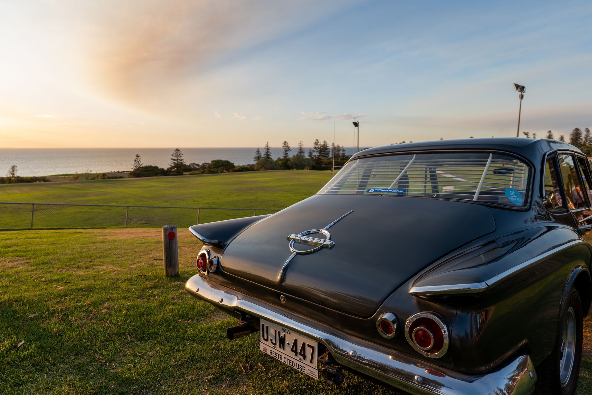 A vintage car is parked in a grassy field with a view of the ocean.
