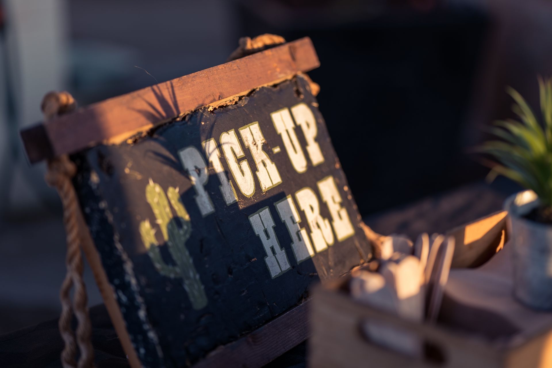 A wooden sign that says pick up here is sitting on a table.