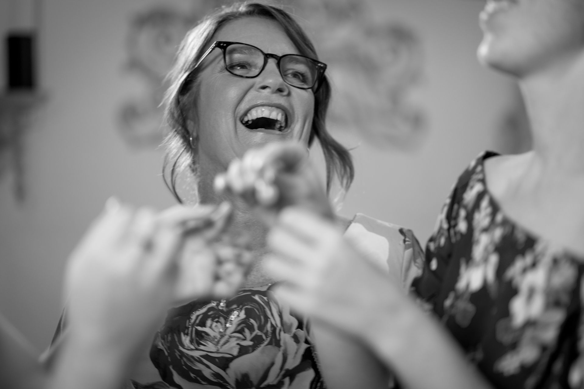 A woman wearing glasses is laughing in a black and white photo.