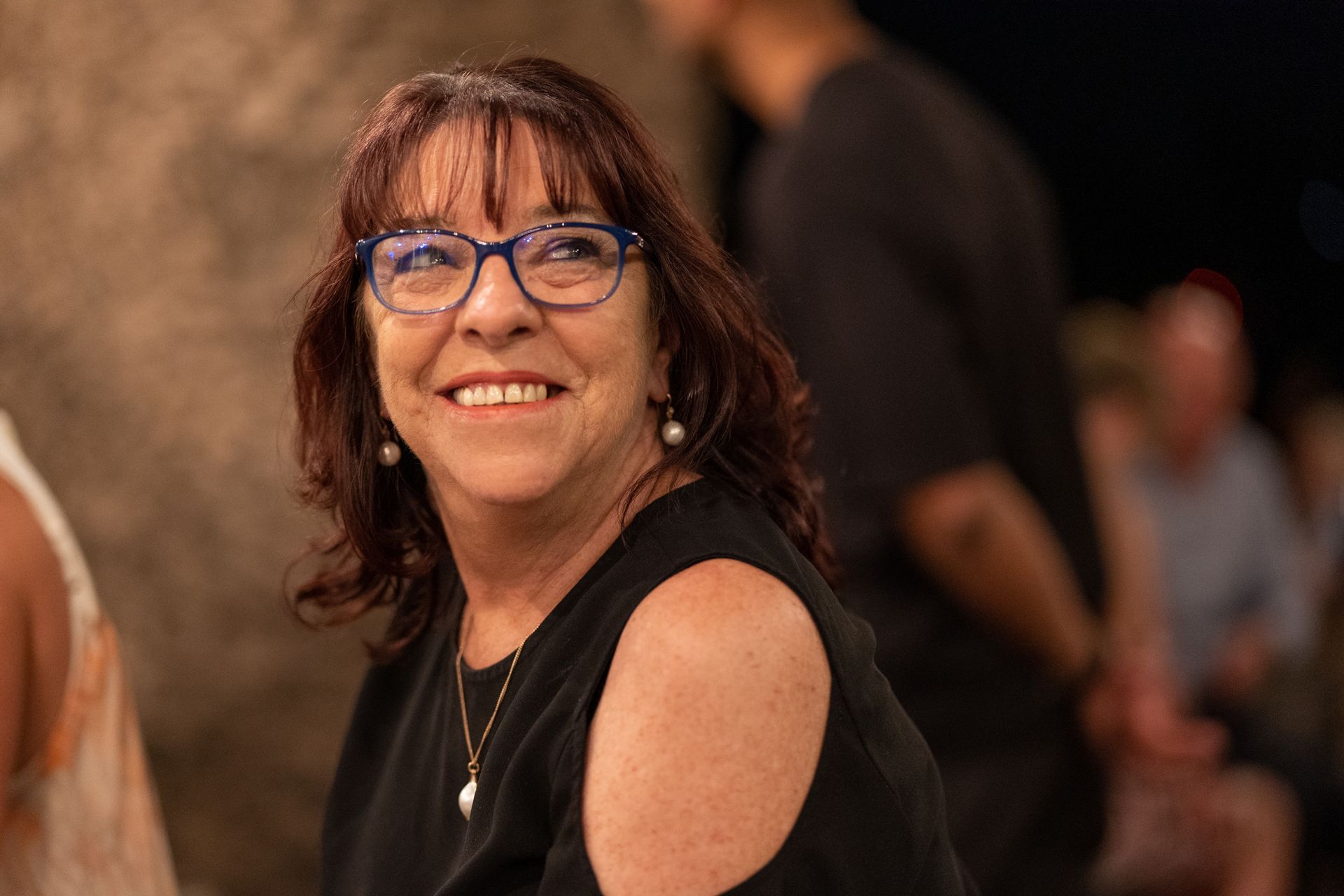 A woman wearing glasses and a black shirt is smiling.