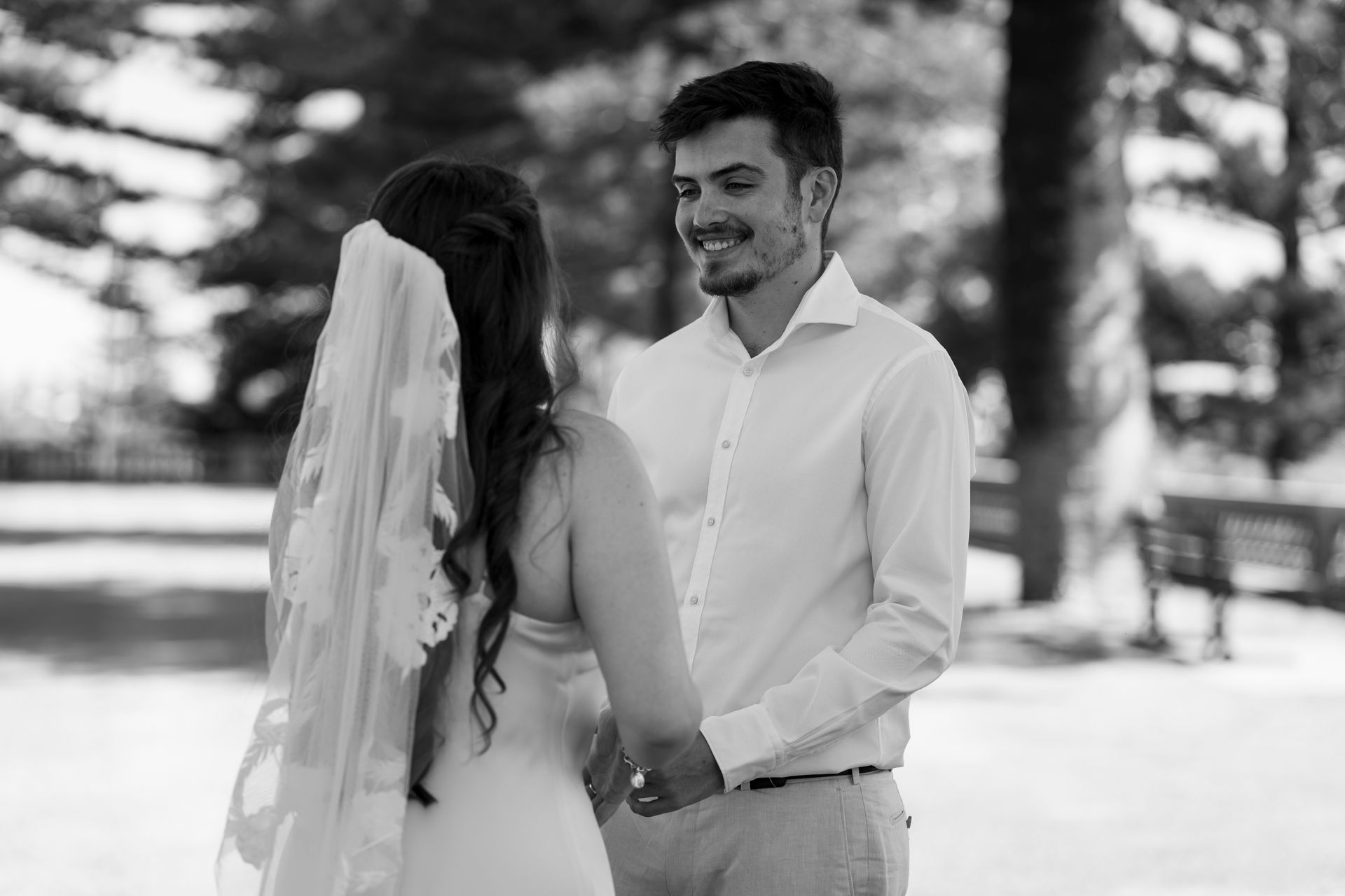 A black and white photo of a bride and groom holding hands in a park.