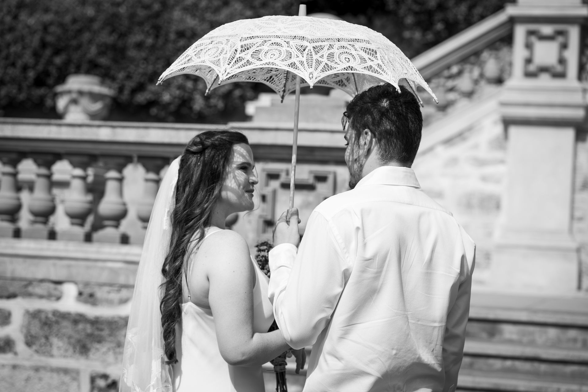 A black and white photo of a bride and groom holding a parasol.