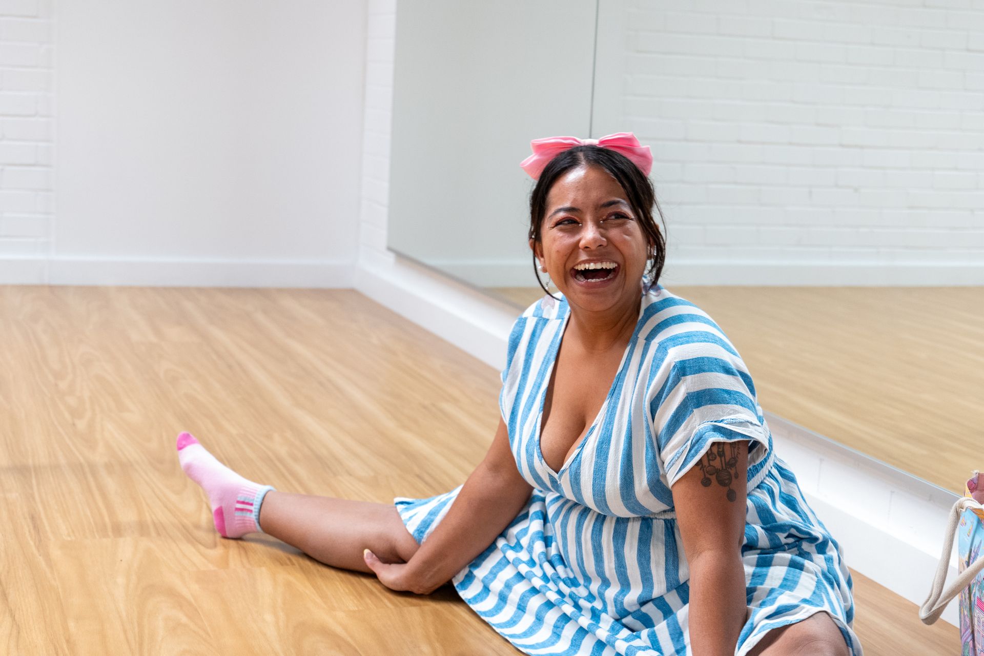 A woman in a blue and white striped dress is sitting on the floor smiling.