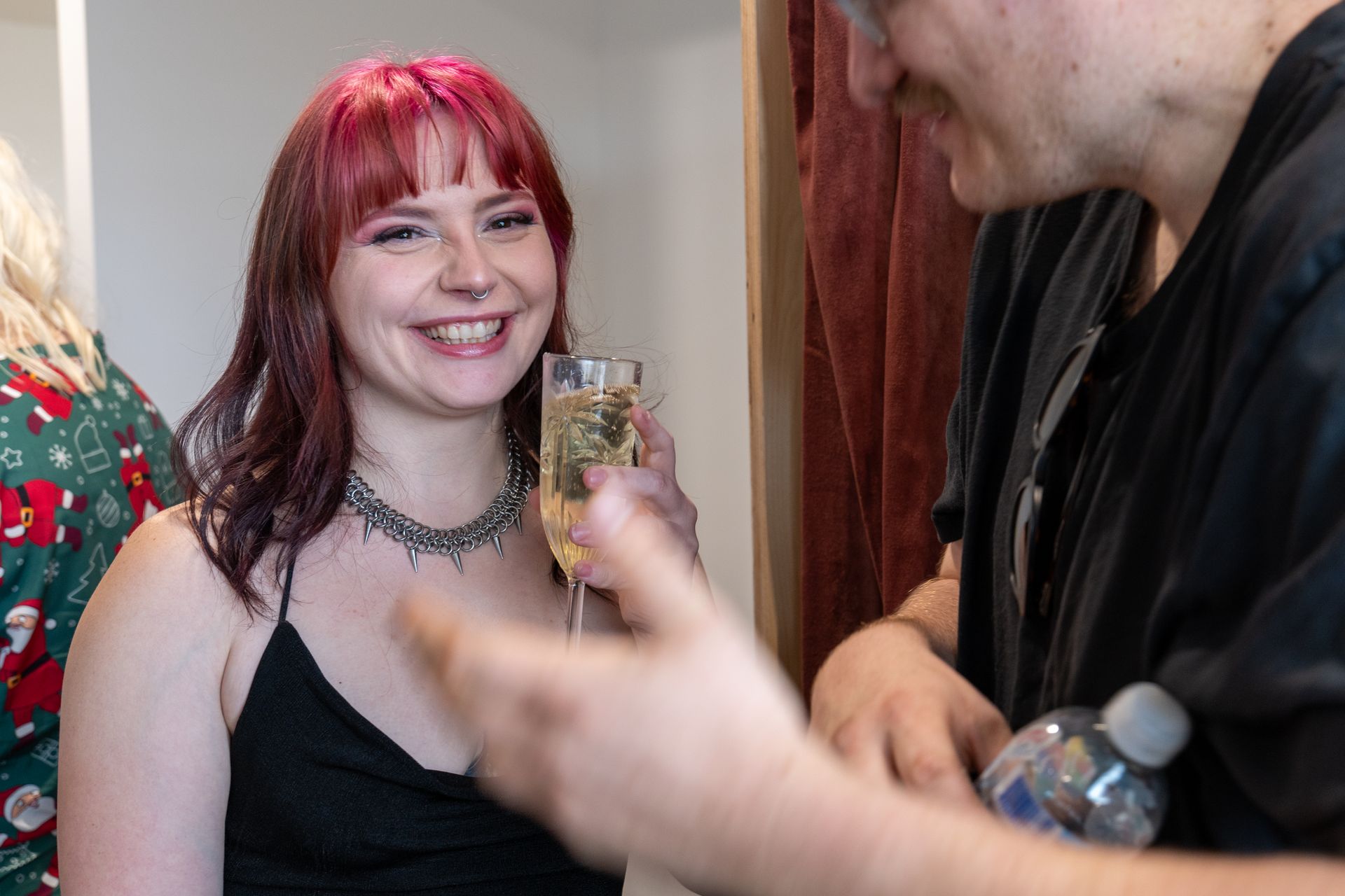 A woman with red hair is smiling while holding a glass of champagne.
