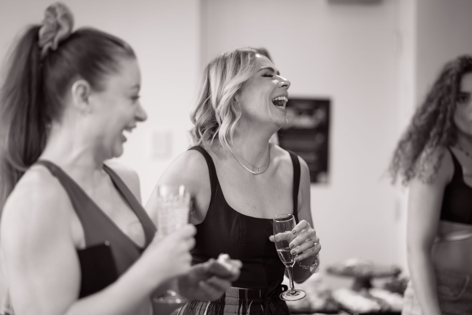 A black and white photo of three women laughing and drinking wine.