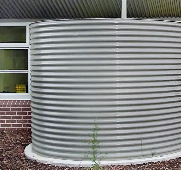 A Large Metal Water Tank Is Sitting in Front of A Brick Building — Maitland Sheet Metal in Rutherford, NSW