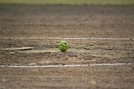Baseball glove with ball on green grass, with blurred baseballs in the background.