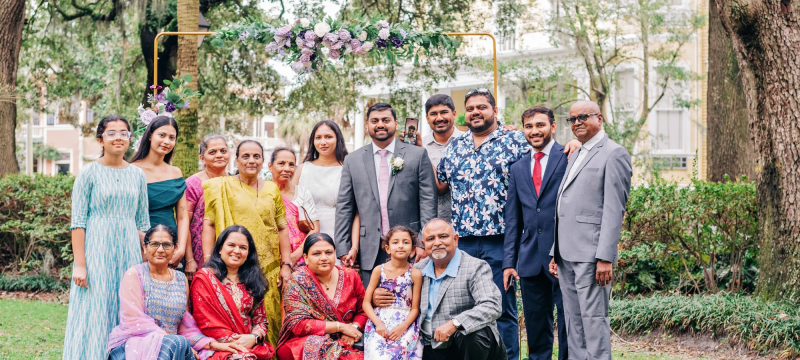 Group portrait of people standing and seated outdoors in a garden, smiling at the camera