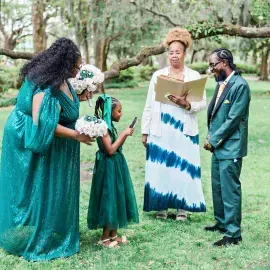 Small outdoor wedding ceremony with four people in green attire in a grassy garden.