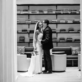 Bride and groom standing together in a modern lounge, holding each other under a veil