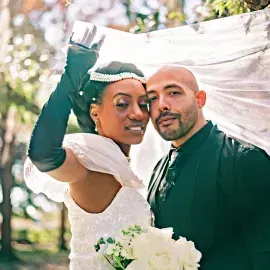 Wedding couple posing outdoors with white bouquet and veil, smiling under soft sunlight