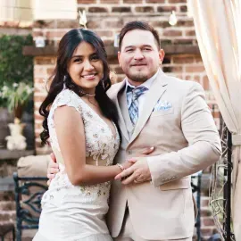 Couple posing outdoors, smiling and holding each other in formal attire.