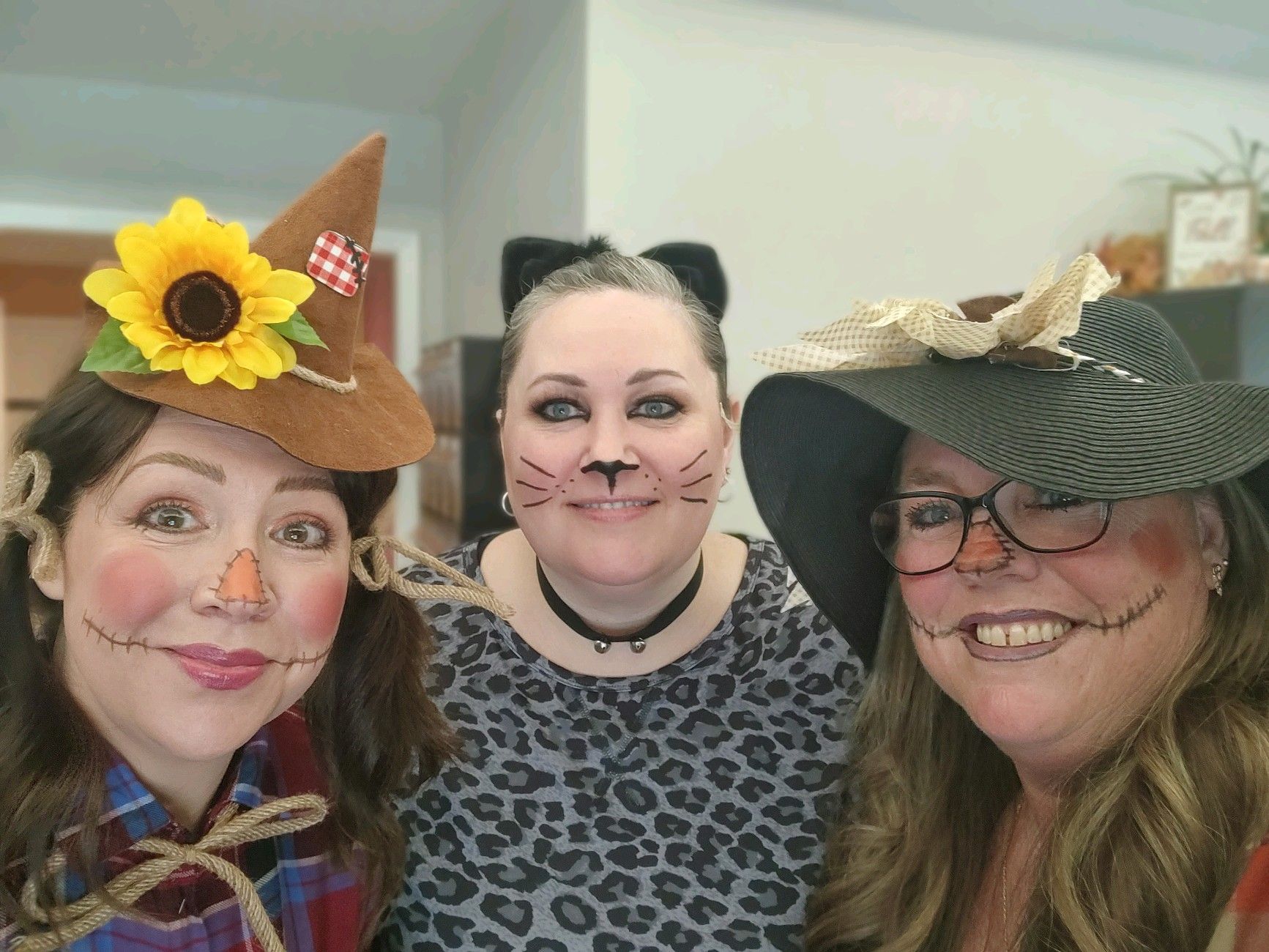 Three women dressed in scarecrow , cat and witch costumes are posing for a picture.