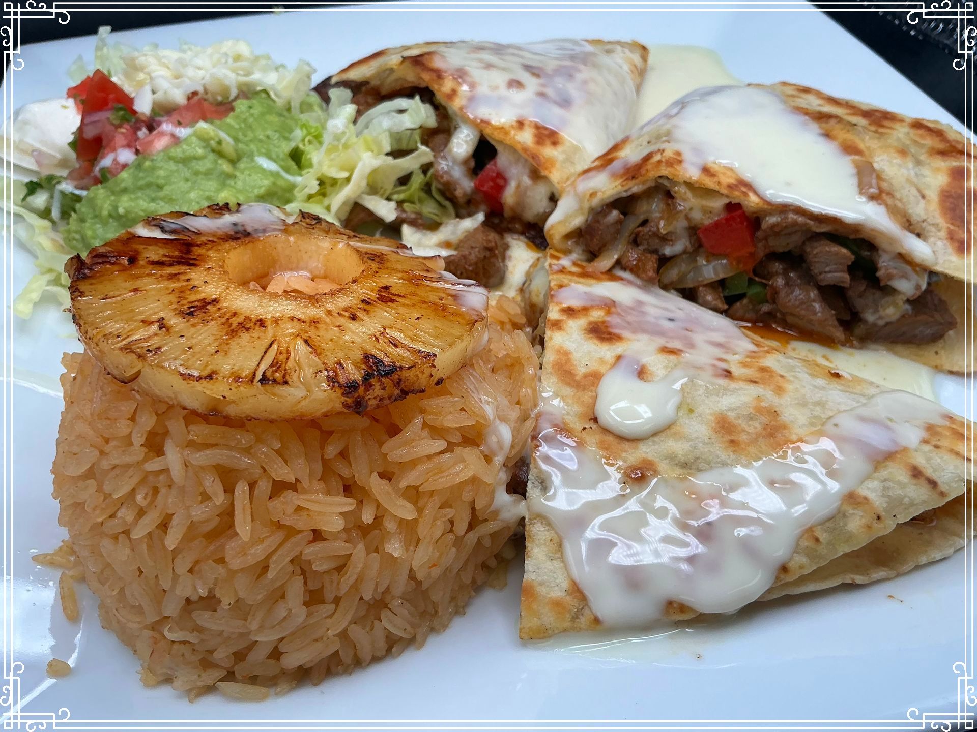 Plate of Mexican food: rice with grilled pineapple, quesadilla, and two burritos with melted cheese.
