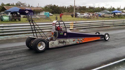 A purple and orange dragster is on a race track