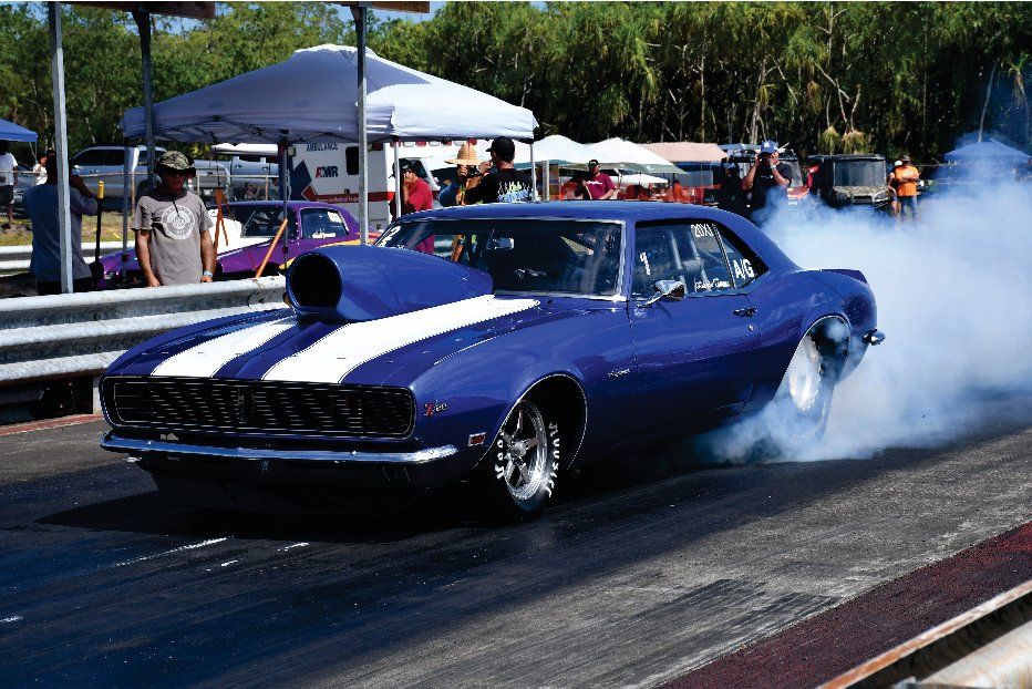 A purple car with white stripes is doing a burnout on a race track