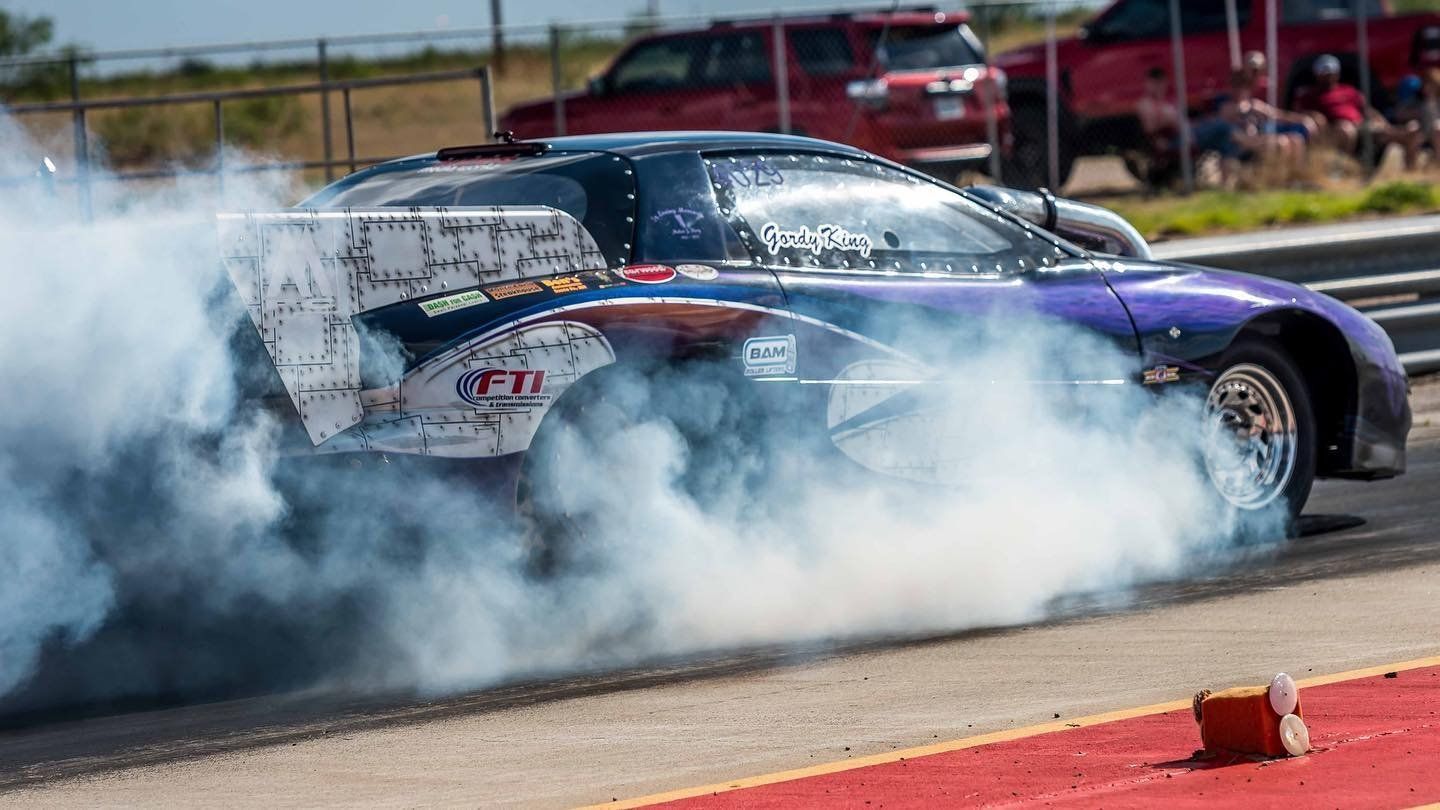 A purple race car is doing a burnout on a track.