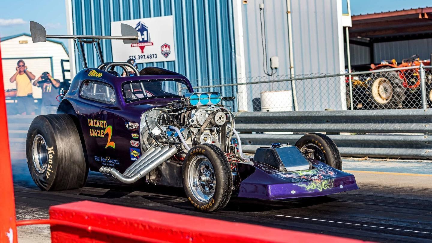 A purple drag car is driving down a race track.