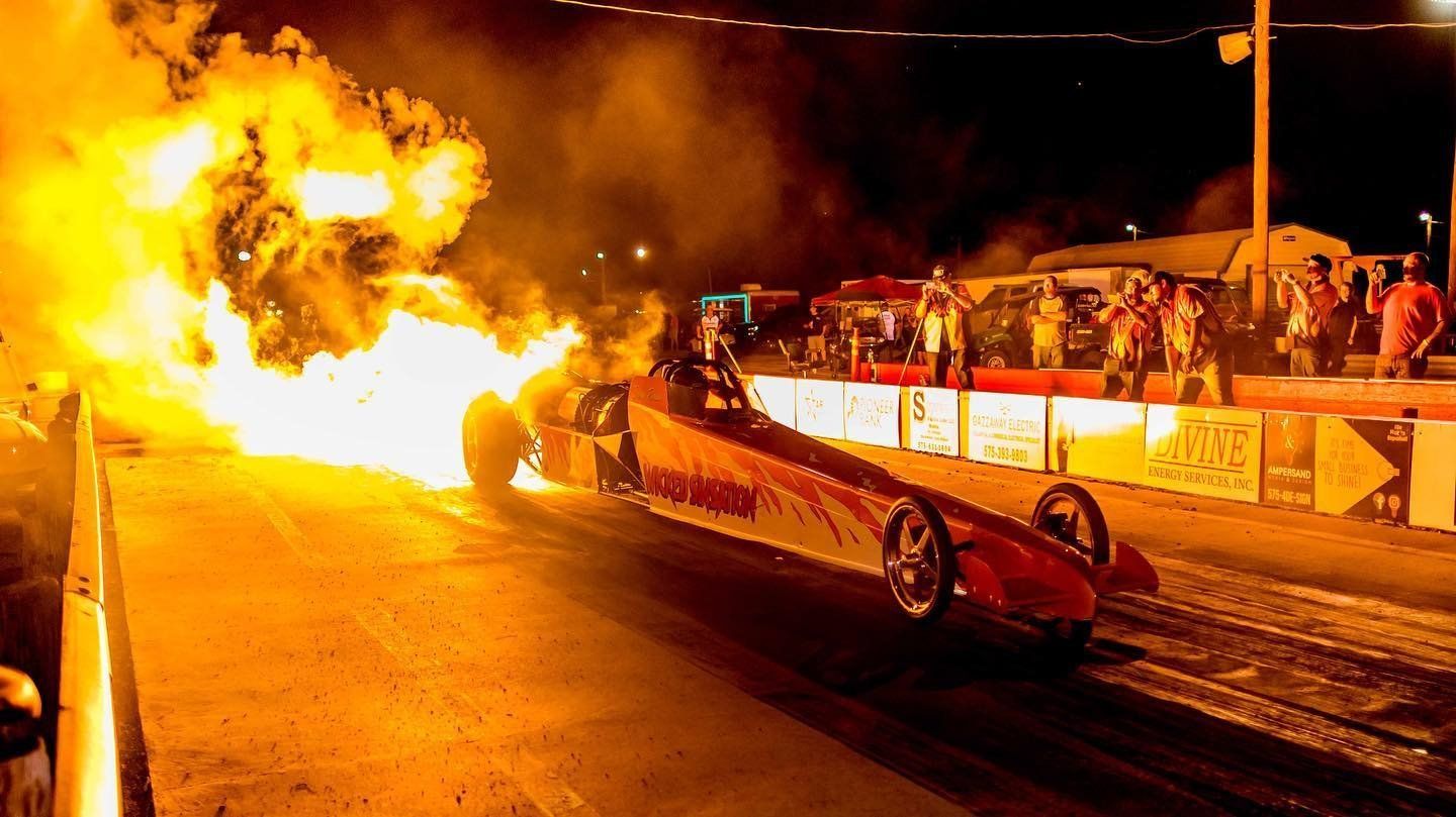 A drag racing car with flames coming out of it is on a track.